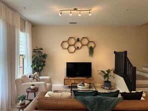 Una sala de estar moderna con un televisor de pantalla plana, una mesa de centro de madera, un sofá y una escalera.