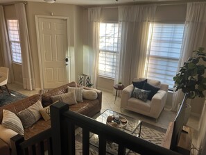 Ein Wohnzimmer mit einem braunen Ledersofa, einem weißen Sofa und einem Glastisch mit Dekoration.