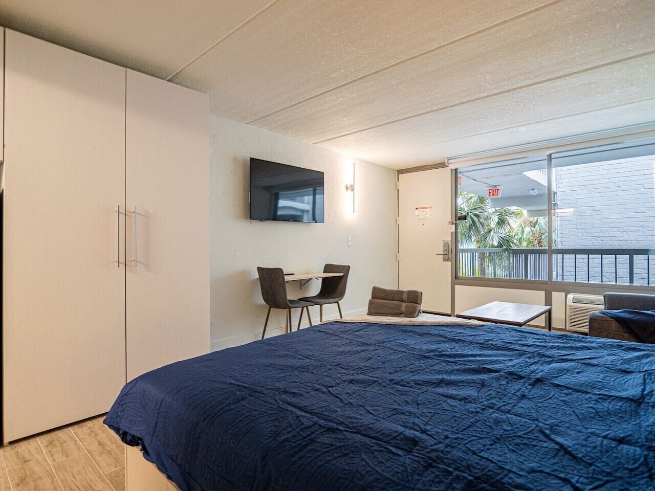 Un dormitorio con una cama grande, un escritorio, dos sillas y un televisor en la pared.