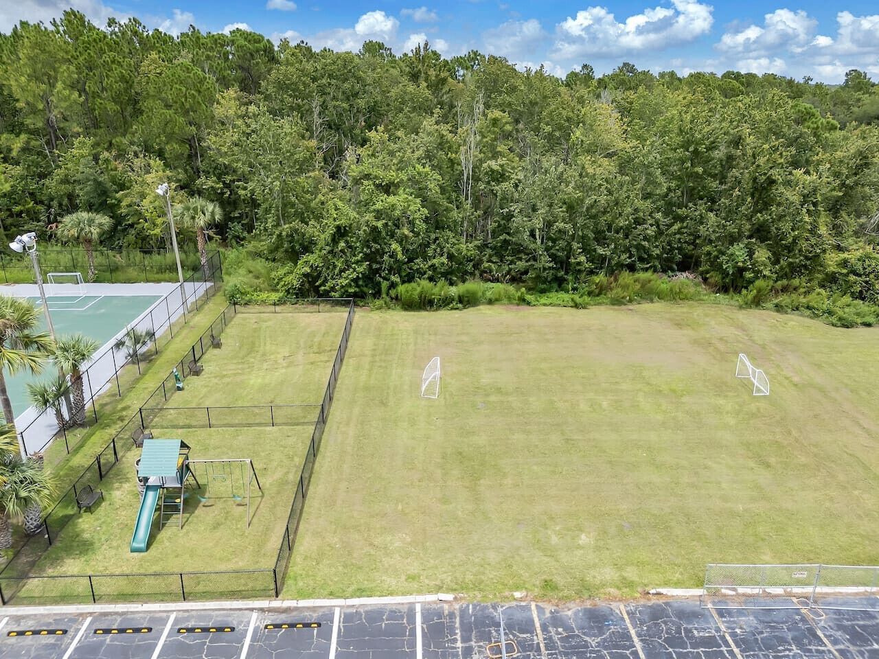 A fenced outdoor area with a playground, a tennis court, and a grassy field.