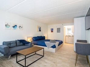 A modern living room with a sofa, a bed, a coffee table, and a dining area. - Bright & Modern Apt Near Disney + Park | Orl (Kissimmee)