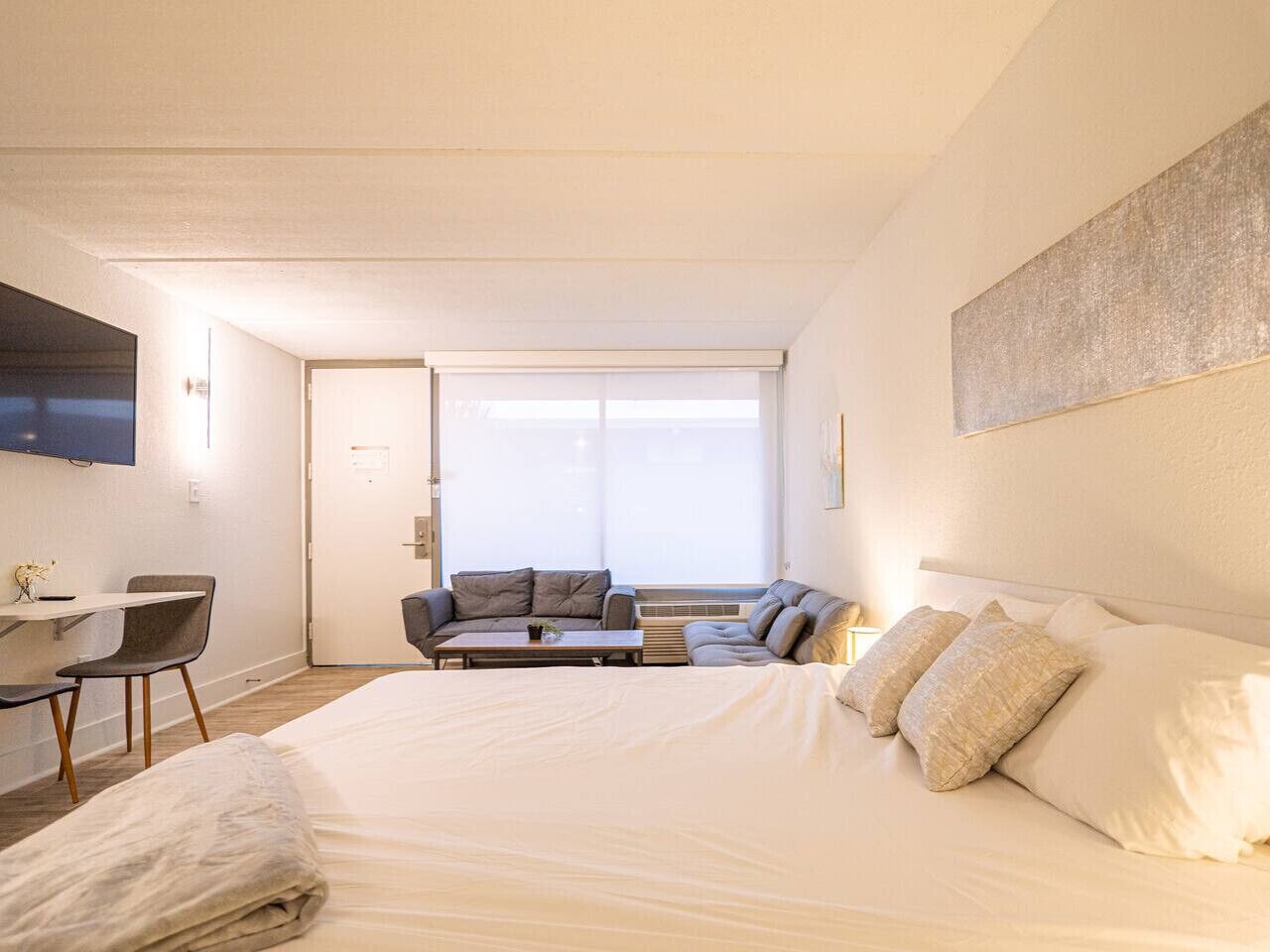 A hotel room with a large bed, a sofa, a coffee table, and a TV mounted on the wall.