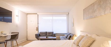 Una habitación de hotel con una cama grande, un sofá, una mesita de centro y un televisor montado en la pared.