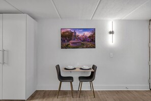 Ein Essbereich mit Tisch und Stühlen, einem Bild an der Wand und einem weißen Kleiderschrank.