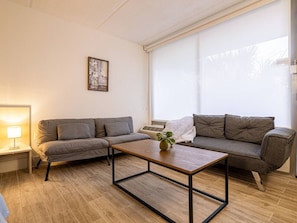 Ein Wohnzimmer mit zwei grauen Sofas, einem Holztisch, einer Lampe und einem Fenster mit Jalousien.