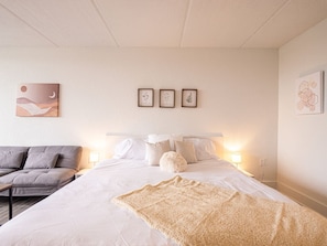 Un dormitorio con cama, almohadas, un edredón, un sofá y decoración en la pared.