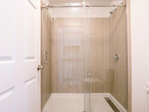 Una ducha a nivel con puerta de vidrio, paredes con azulejos y un marco de puerta blanco.