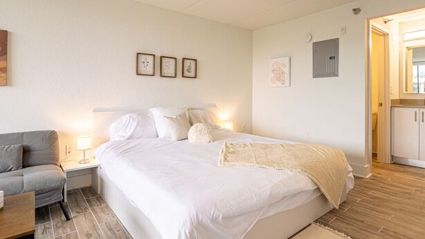 Ett sovrum med en säng, ett sängbord, en lampa och en grå soffa.