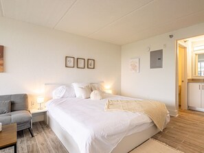 A bedroom with a bed, bedside table, lamp, and a grey sofa. - Modern Suite - 7 Min to Disney World & Universal (Kissimmee)