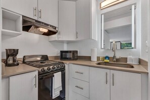 A modern kitchen with a gas stove, a microwave, and a coffee maker. - Snug Studio 8 min to Disney w Pool & Parking | Orl (Kissimmee)