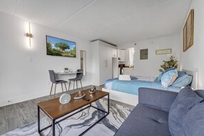 A modern living room with a sofa, a coffee table, and a dining area with chairs. - Snug Studio 8 min to Disney w Pool & Parking | Orl (Kissimmee)