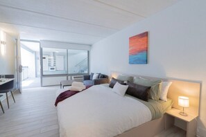 Un dormitorio moderno con una cama grande, mesitas de noche, un escritorio y vistas al balcón.