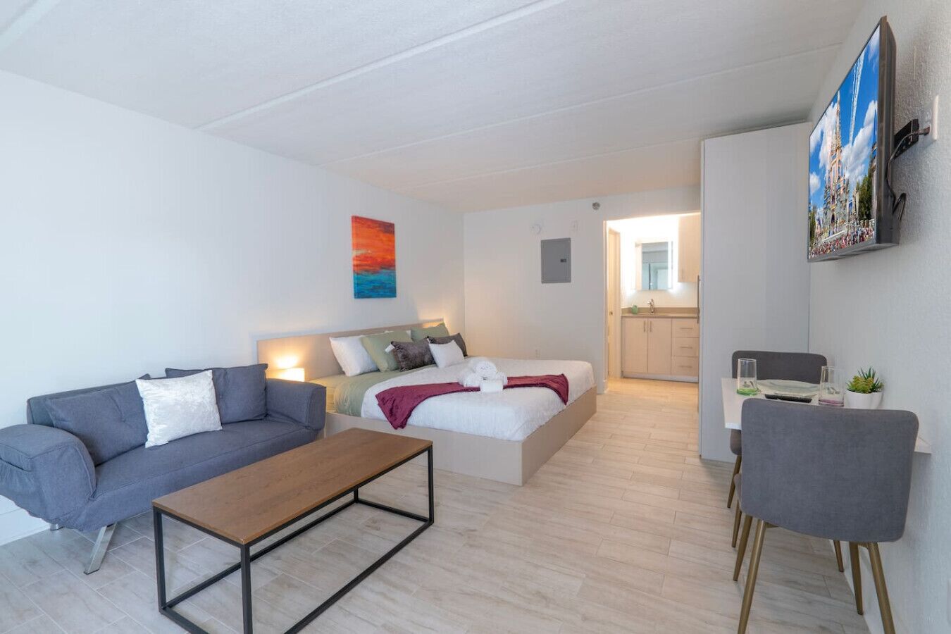 Een moderne slaapkamer met een bed, een grijze bank, een houten salontafel en een grijze fauteuil.