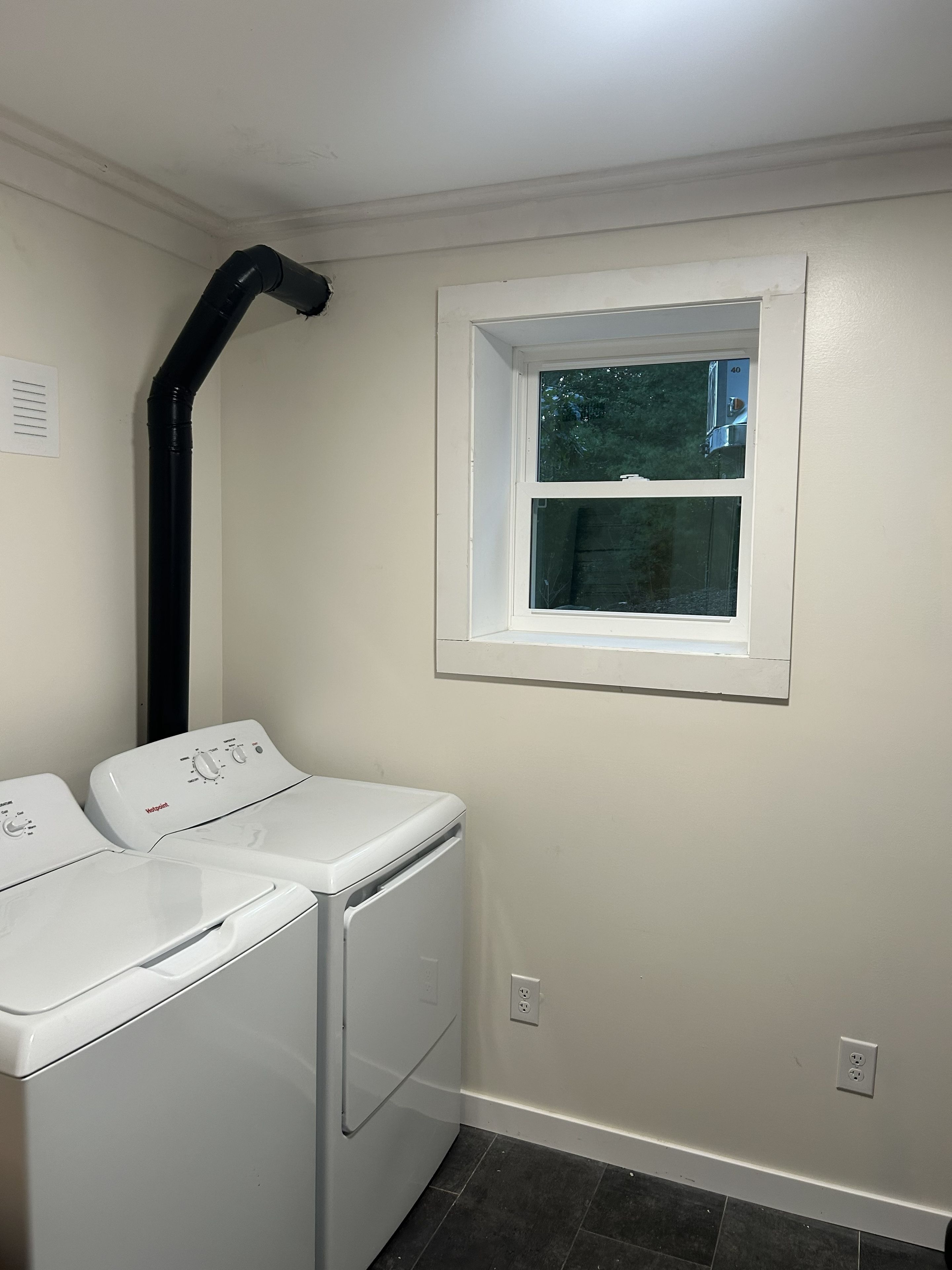 A laundry room with two white front-loading washers and a black vent pipe.