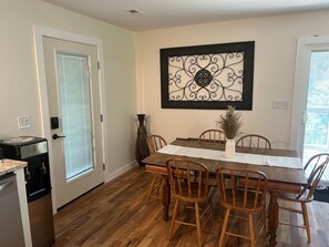 A dining area with a wooden table, six chairs, a vase, and a decorative metal piece on the wall. - Private 3-bedroom cottage 6 acres in charming Crumpler with AC, large deck (Crumpler)