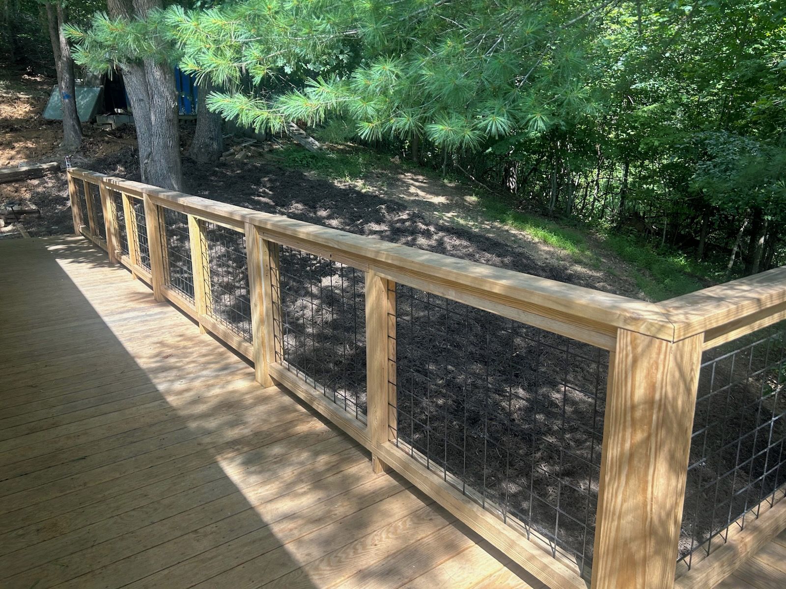 A wooden deck with a metal fence and dense foliage in the background.