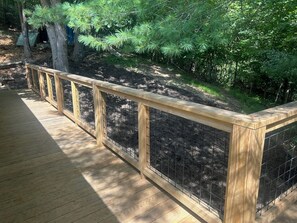 Eine Holzterrasse mit einem Metallzaun und dichtem Grün im Hintergrund.