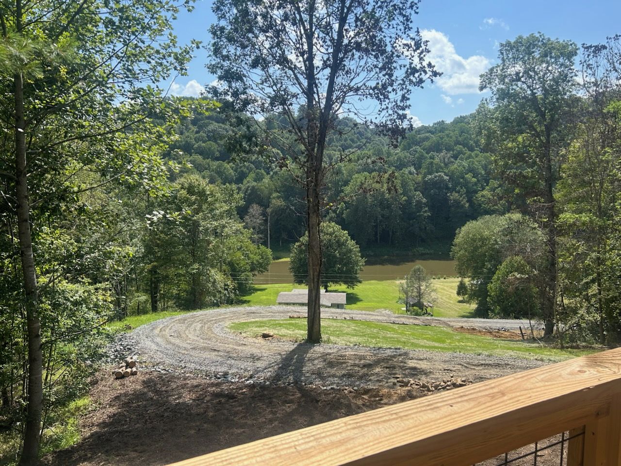 Una terraza de madera con vistas a un sendero de tierra, un área boscosa y un edificio pequeño a lo lejos.