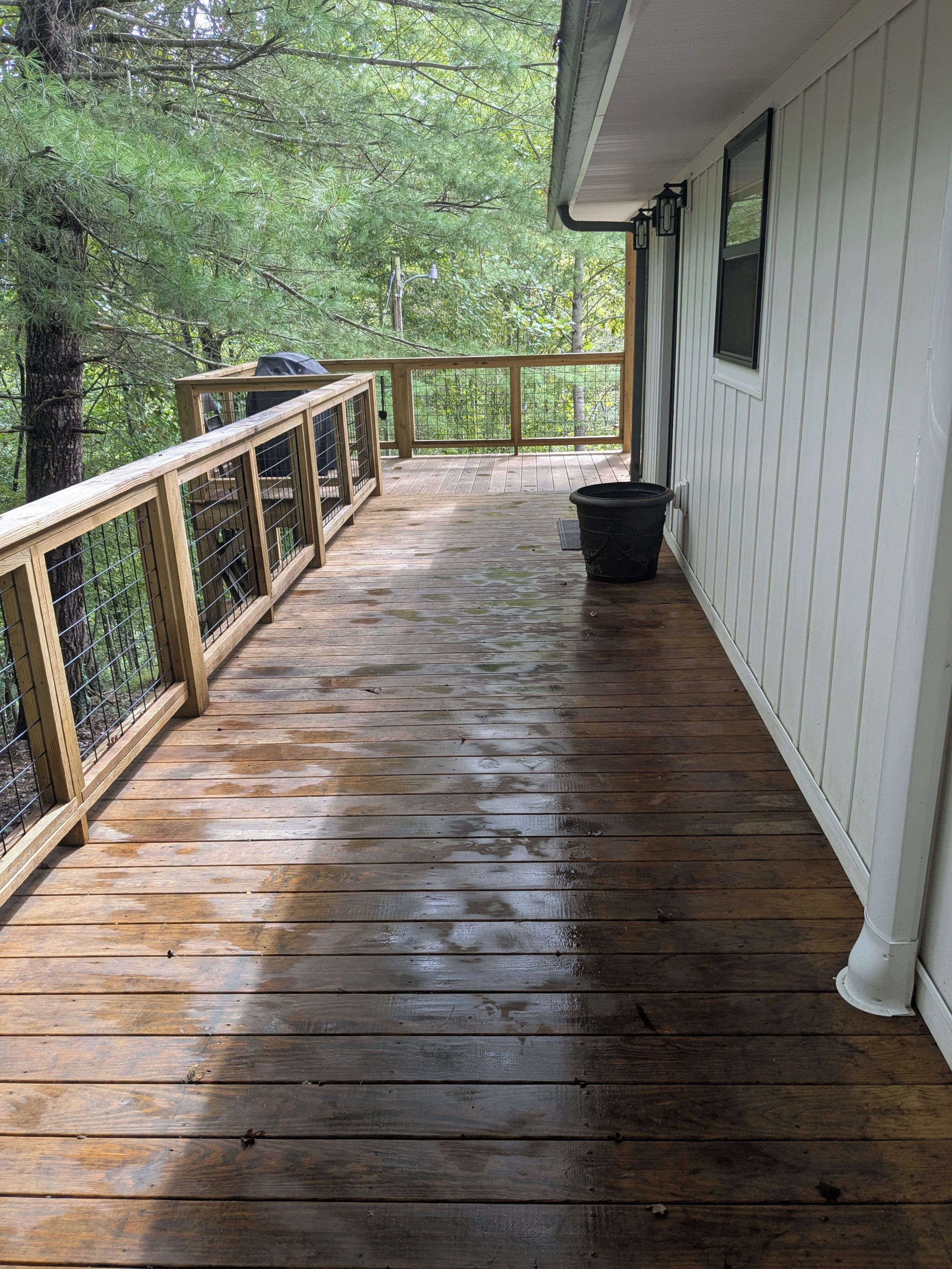 A wooden deck with a railing, a trash bin, and a covered area with a grill.