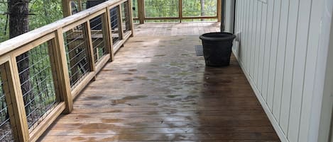 A wooden deck with a railing, a trash bin, and a covered area with a grill.