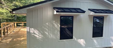 A white building with a gabled roof, two windows, and a deck.