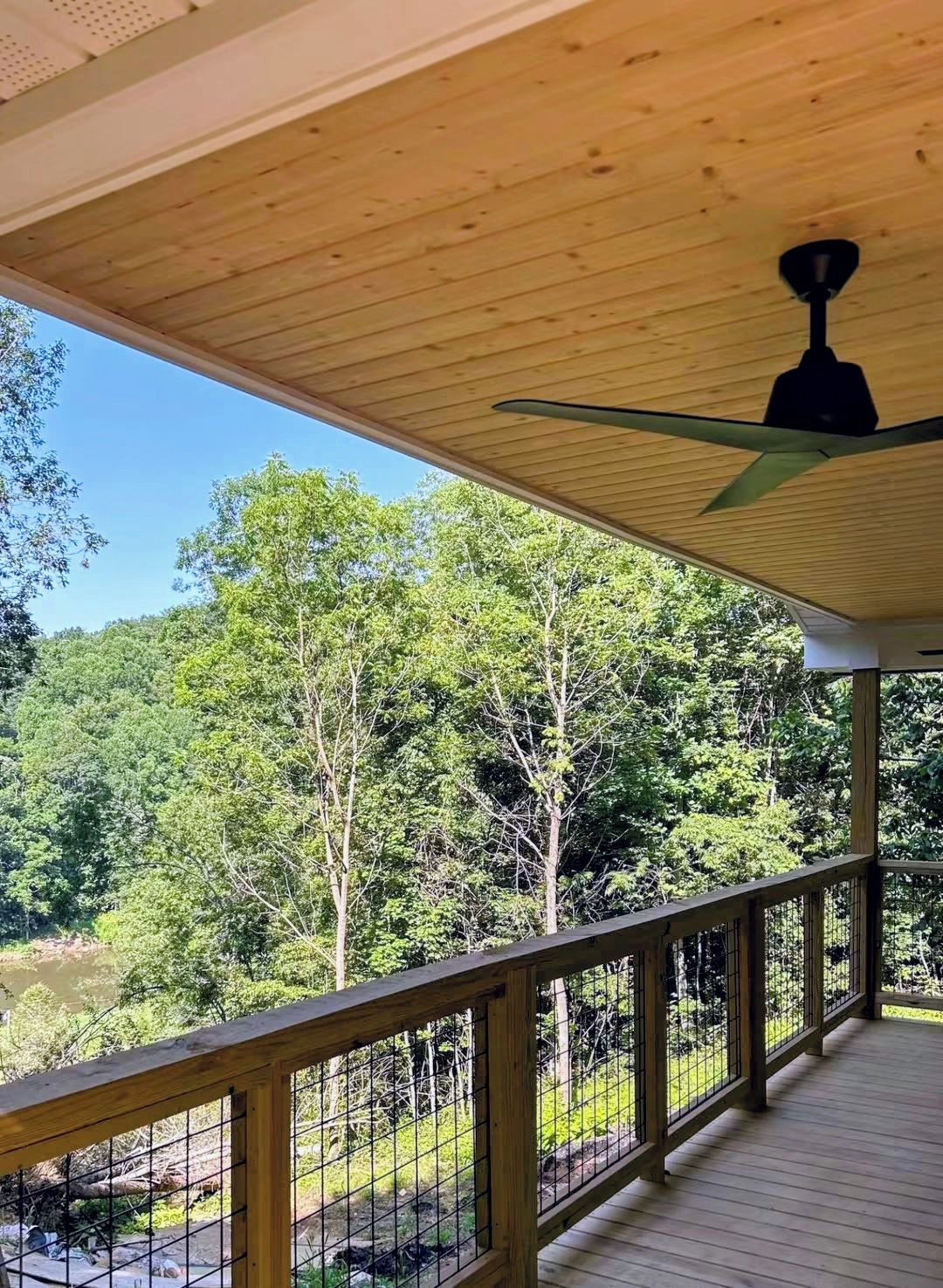 Terraza de madera con ventilador de techo, con vista a un área boscosa.
