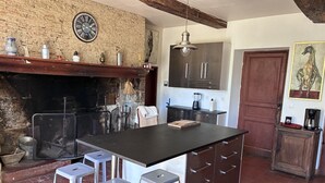 Una cuina amb una illa gran, tamborets de bar, un llum penjant i una paret de maó rústica.