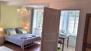 A bedroom with a bed, bedside tables, a chandelier, and a view of the outdoors through a window.