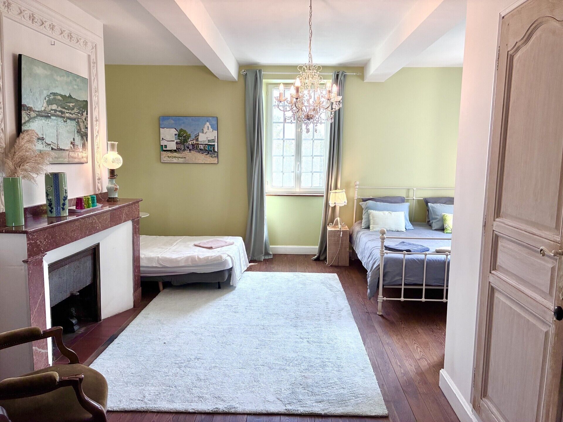 A bedroom with a bed, a chair, a fireplace, and a chandelier.