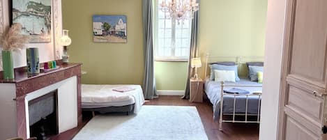 A bedroom with a bed, a chair, a fireplace, and a chandelier.
