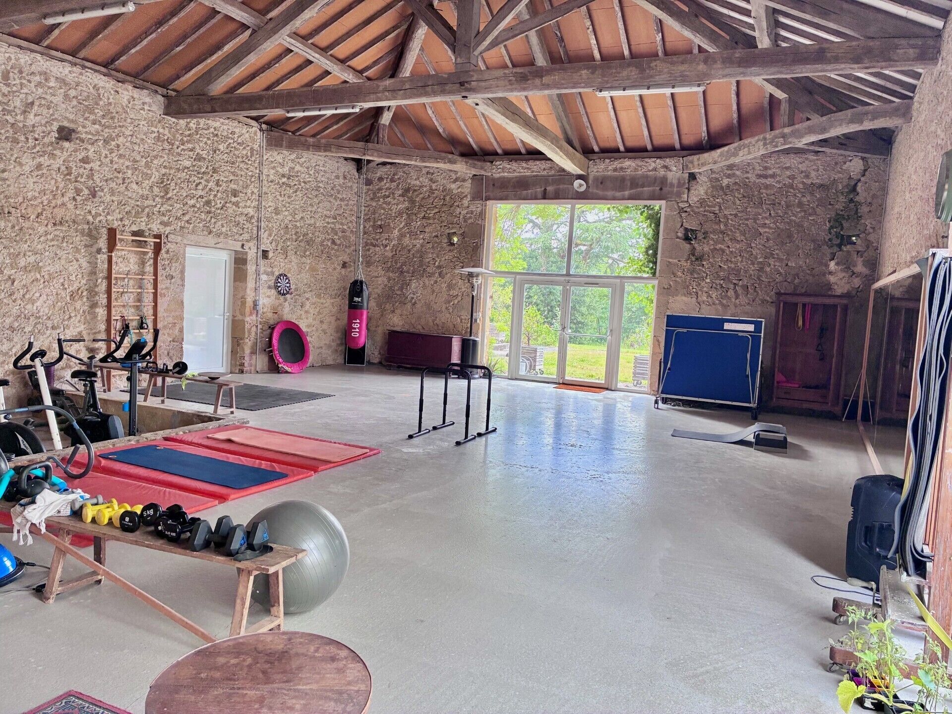 A spacious indoor gym with various exercise equipment, a large window, and a rustic stone wall.