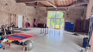 A spacious indoor gym with various exercise equipment, a large window, and a rustic stone wall.