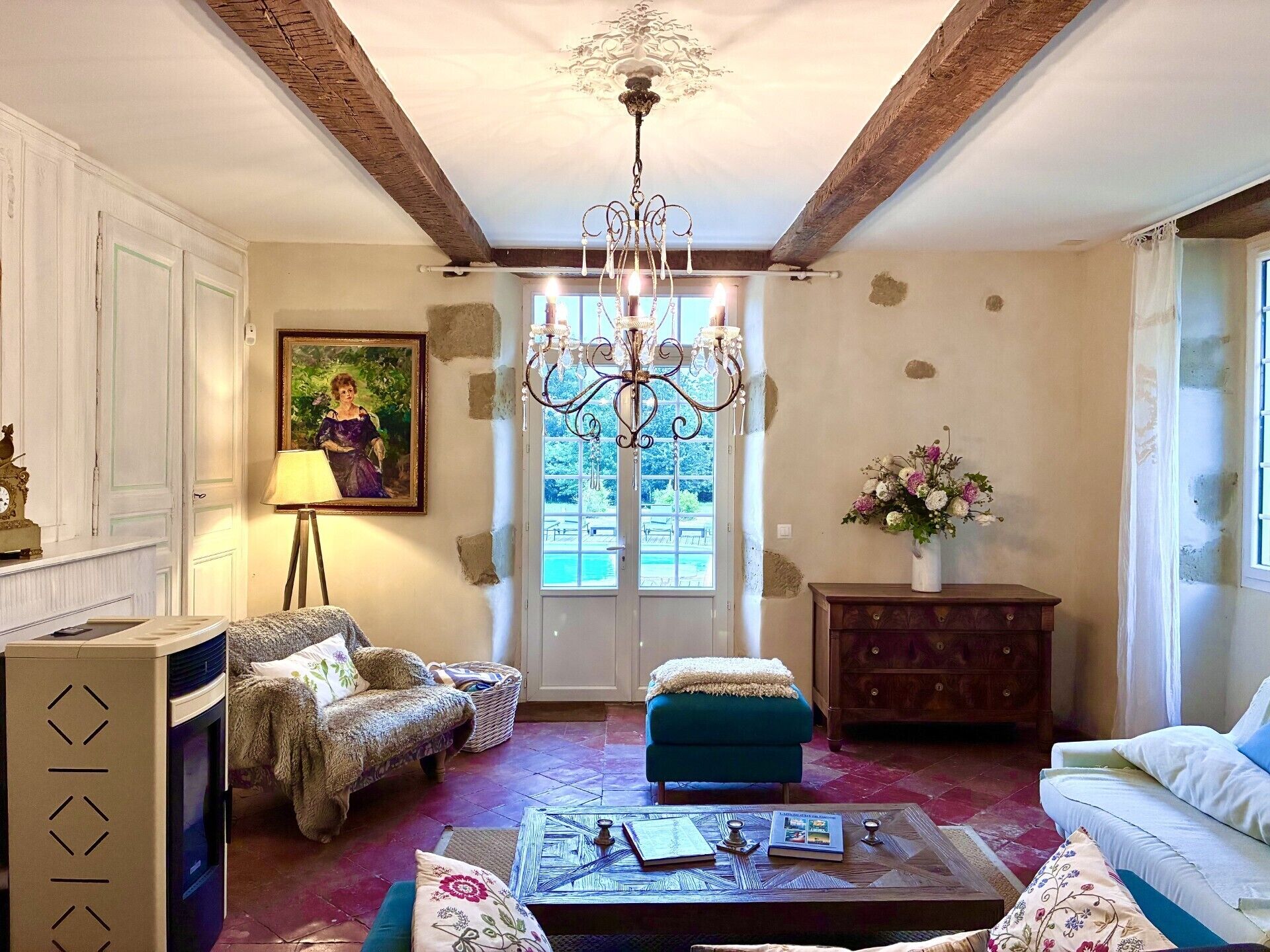 A living room with a chandelier, a painting, a sofa, a coffee table, and a view through a window.