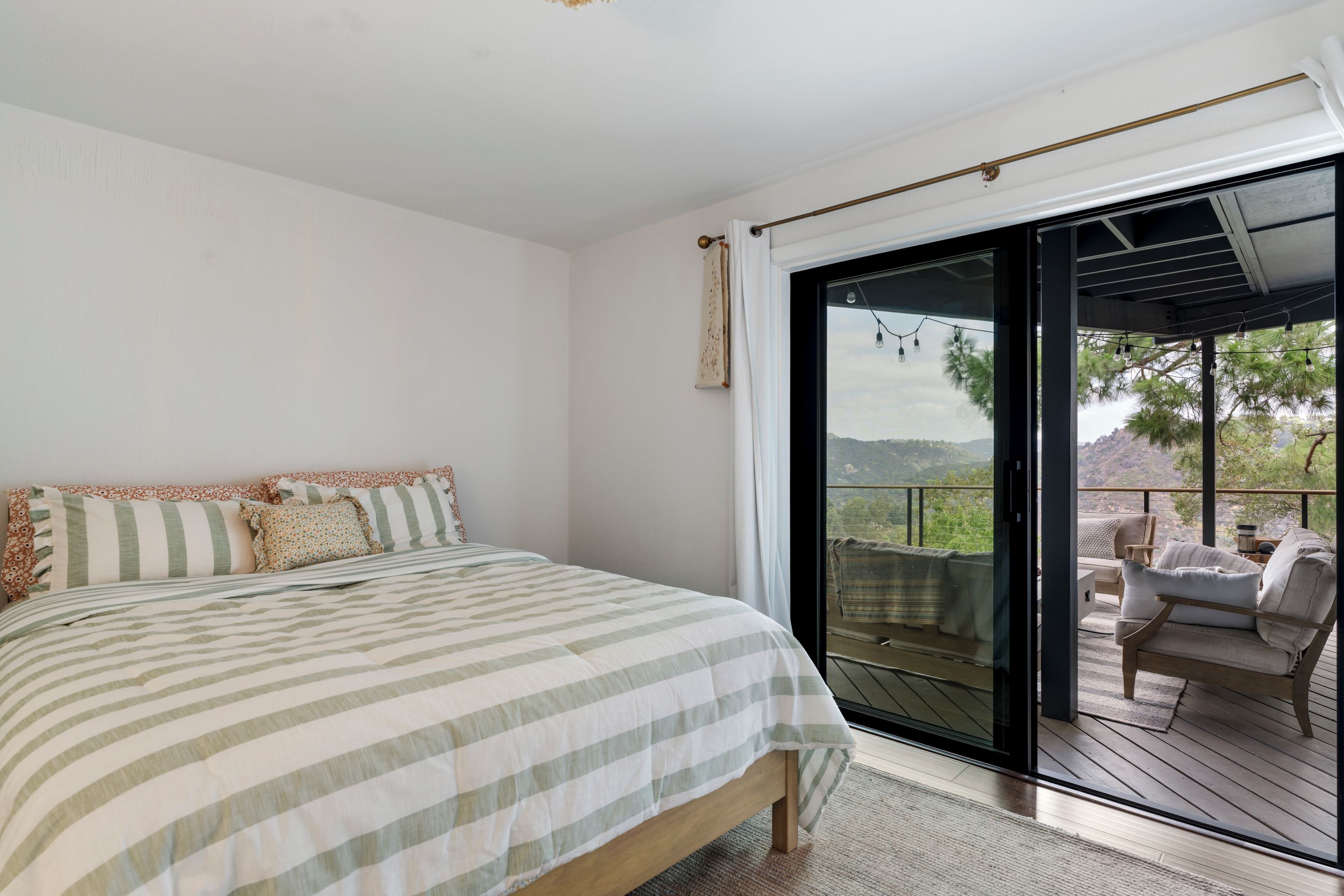 A bedroom with a large bed, a sliding glass door leading to an outdoor deck with seating.