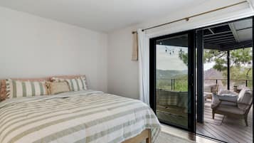A bedroom with a large bed, a sliding glass door leading to an outdoor deck with seating.