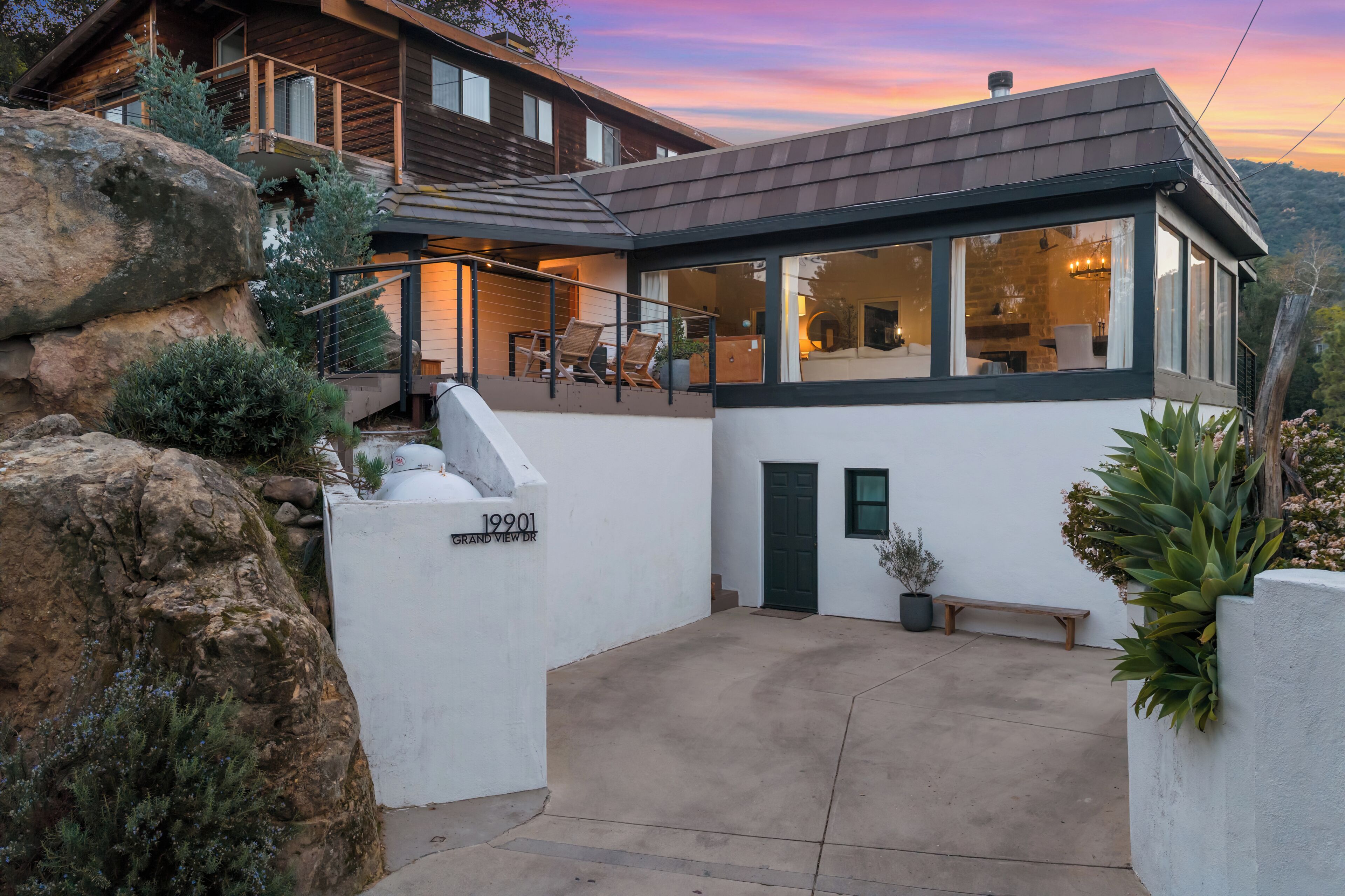 A modern house with a covered patio, a stone wall, and a view of the surrounding landscape.