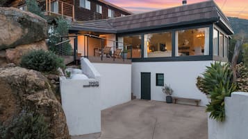 A modern house with a covered patio, a stone wall, and a view of the surrounding landscape.
