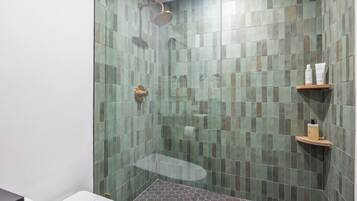 A shower area with a glass door, a handheld showerhead, and a shelf with toiletries.