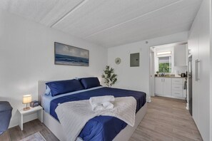 Un dormitorio con cama, mesita de noche, lámpara y vistas a la cocina.
