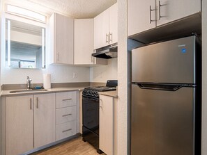 A compact kitchen with a stainless steel refrigerator, a gas stove, and light-colored cabinets. - Cozy Unit Near Disney World + Free Parking | Orl (Kissimmee)