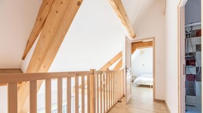 A room with a sloped ceiling, wooden beams, a white door leading to another room, and a bed with a white cover. - La Banne - SAINT SAUVES D'AUVERGNE (SAINT SAUVES D'AUVERGNE)