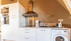 A compact kitchen with a built-in oven, a stainless steel range hood, a coffee maker, and a washing machine. - La Banne - SAINT SAUVES D'AUVERGNE (SAINT SAUVES D'AUVERGNE)