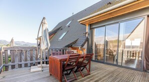 A wooden deck with a table and chairs, a glass sliding door, and a view of the mountains. - La Banne - SAINT SAUVES D'AUVERGNE (SAINT SAUVES D'AUVERGNE)