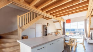 Eine moderne Küche mit einer Holztreppe, einem Essbereich mit Tisch und Stühlen sowie einem großen Fenster mit Blick ins Freie.