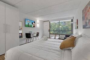 A hotel room with a large bed, a desk with two chairs, a television, and a window with a view of trees. - Cozy Modern King Room Close to Disney + Pool | Orl (Kissimmee)