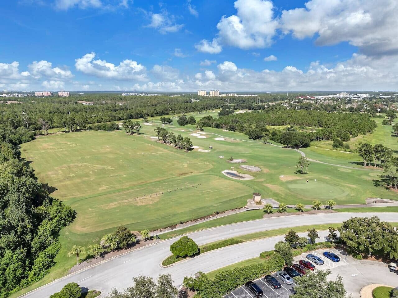 A golf course with a parking area and buildings in the background.