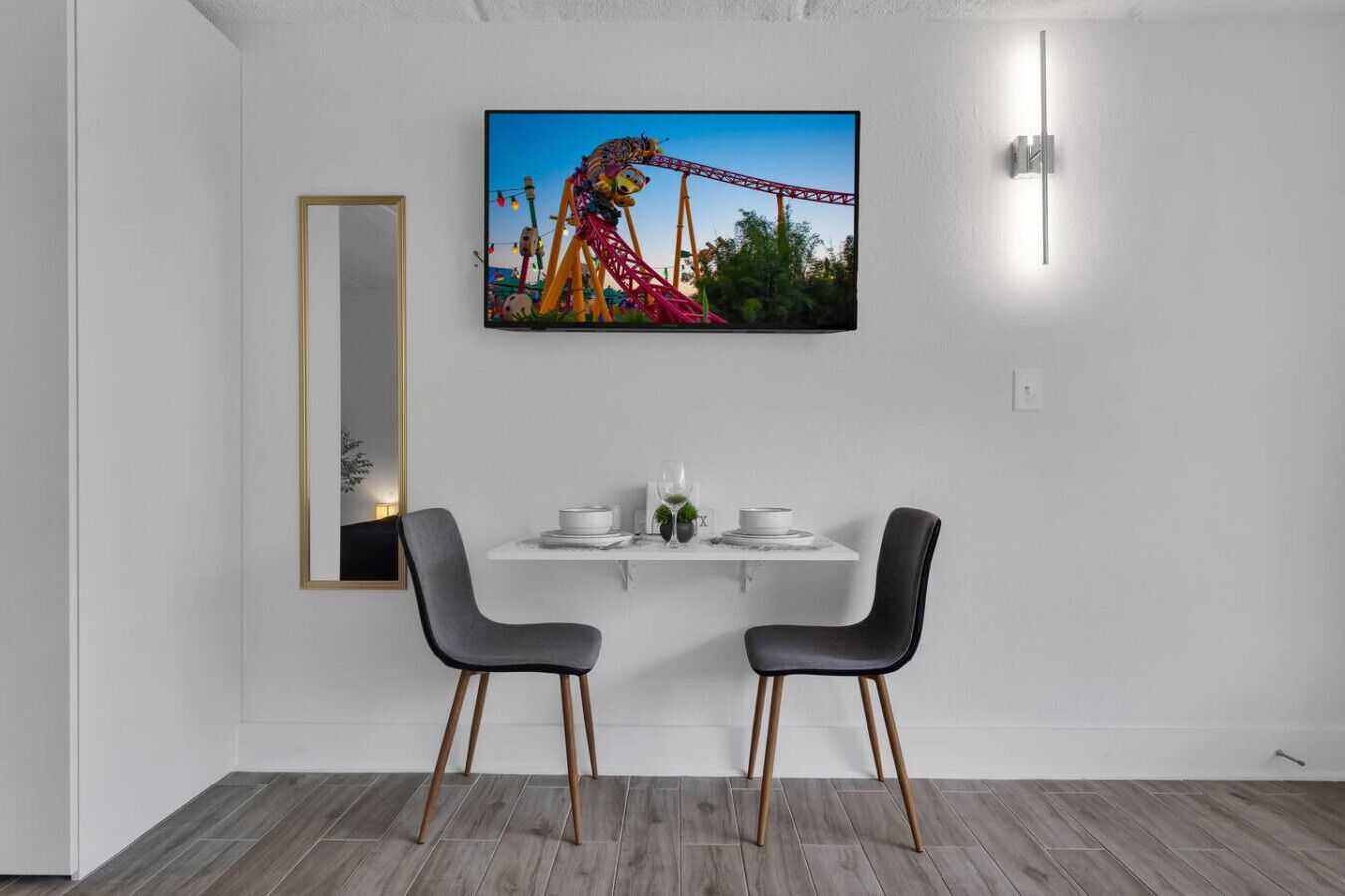 Un coin repas moderne avec une table blanche, deux chaises, un tableau encadré au mur et un miroir.