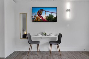 Un coin repas moderne avec une table blanche, deux chaises, un tableau encadré au mur et un miroir.