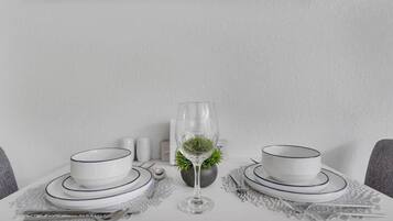 Une table dressée avec de l’assiette et des bols blancs, un verre d’eau, et une petite plante au centre.