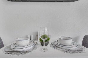 Une table dressée avec de l’assiette et des bols blancs, un verre d’eau, et une petite plante au centre.